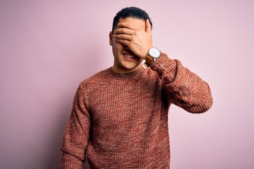 Young brazilian man wearing casual sweater standing over isolated pink background smiling and laughing with hand on face covering eyes for surprise. Blind concept.