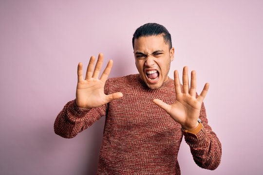 Young brazilian man wearing casual sweater standing over isolated pink background showing and pointing up with fingers number ten while smiling confident and happy.