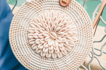 Trendy round crossbody straw bag with seashells on the beautiful lounge chair near a pool. Summer outfit, vacation, holiday concept. Travel background with place for text, close up