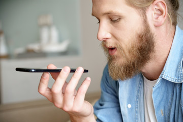 Young man hold phone speak on speakerphone using virtual digital voice recognition assistant search...