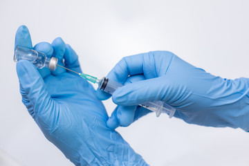 Hand wearing a disposable glove filling a syringe with dosage from a vial.