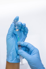 Hand wearing a disposable glove filling a syringe with dosage from a vial.