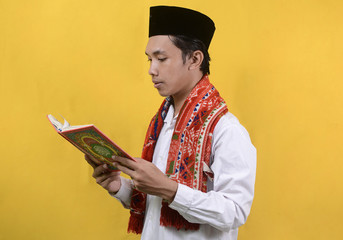 A man holds the Quran in his hand with a yellow background
