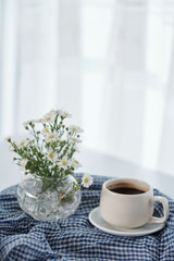 Fototapeta na wymiar Vase with blooming flowers and cup of tasty black coffee on table