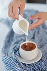 Hands of woman pouring milk in cup of black coffee in the morning