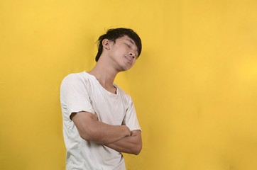 portrait of Asian man wearing a white shirt with a sleep expression isolated on a yellow background
