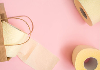 Three rolls of toilet paper with a craft bag for shopping and goods on a pink background.