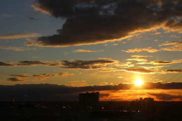 Red sun at sunset or dawn at dusk low above the horizon shrouded in smoke from the chimneys of the plant.