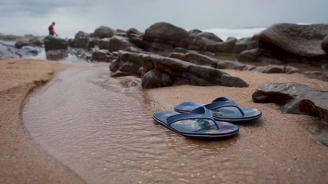 Colourful flip flops in sea water with rocks and ocean in background.