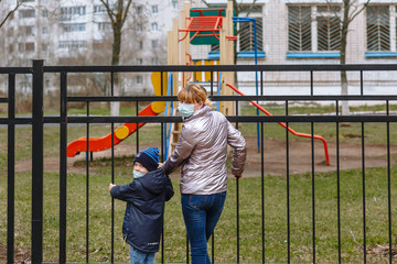 Naklejka premium Mother and child in medical masks suddenly turned around. On the background of a Playground behind a metal fence.