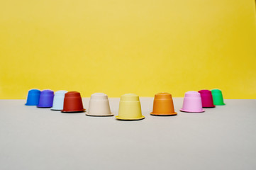 Multi-colored coffee capsules for coffee-machine are lined up with the letter V on a gray-yellow background