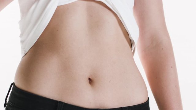 Close-up of a girl's fit and slim belly as she lifts her shirt to show her bare stomach.
