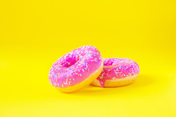 A stack of donuts with pink icing on a yellow background side view. Junk food. Sweets, pastries. Calories, fat.