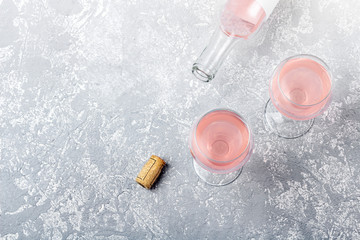 Rose wine tasting layout. Opened bottle and two glasses with rose wine on a grey background. Drunkenness concept. Top view, flat lay,  copy space for text