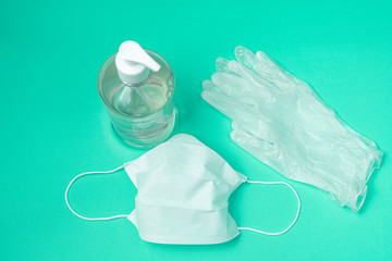 Container with alcohol gel, gloves and surgical mask on the light blue background