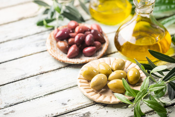 Variety of black and green olives and olive oil in bowls on white background close up