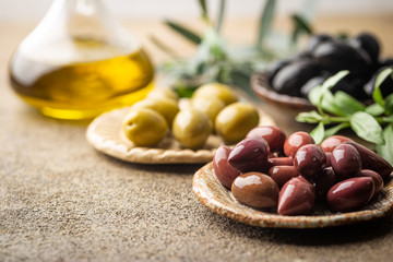 Variety of black and green olives and olive oil in bowls on stone background close up