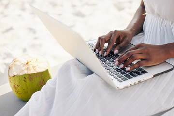 Close-up image of young woman spending time on sandy beach and working on laptop