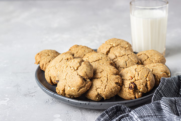 Healthy vegan cookies with nuts and raisin on a ceramic plate with milk, grey concrete background. Dessert or breakfast for children, sweet snack. Selective focus. 