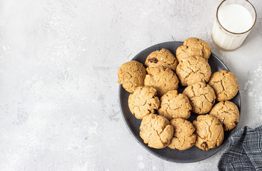 Healthy vegan cookies with nuts and raisin on a ceramic plate with milk, grey concrete background. Dessert or breakfast for children, sweet snack. Selective focus. Top view.