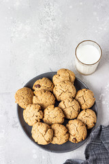 Healthy vegan cookies with nuts and raisin on a ceramic plate with milk, grey concrete background. Dessert or breakfast for children, sweet snack. Selective focus. Top view.