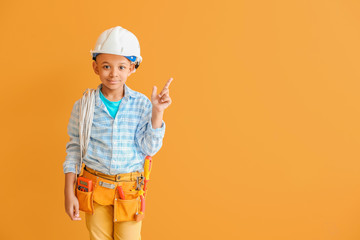 Little African-American electrician pointing at something on color background