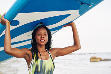 Attractive sensual young woman carrying surfboard over her head when walking out of sea