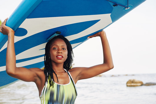 Attractive sensual young woman carrying surfboard over her head when walking out of sea