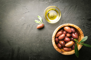 Black olives and olive oil in wooden bowls on black background. Top view with copy space for text.