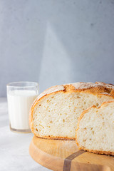 Sliced loaf of freshly baked artisan sourdough bread and a glass of milk. No knead bread. Light grey concrete background.