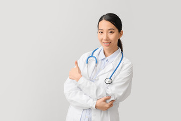 Female Asian doctor showing thumb-up on light background