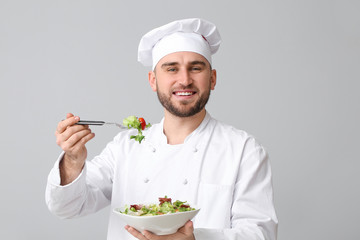 Handsome male chef with salad on light background