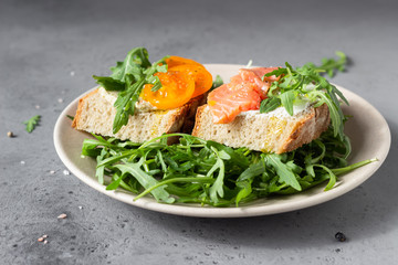 Healthy open sandwiches with artisan bread with cream cheese, salmon, tomatoes and arugula on ceramic plate. Balanced diet concept. 