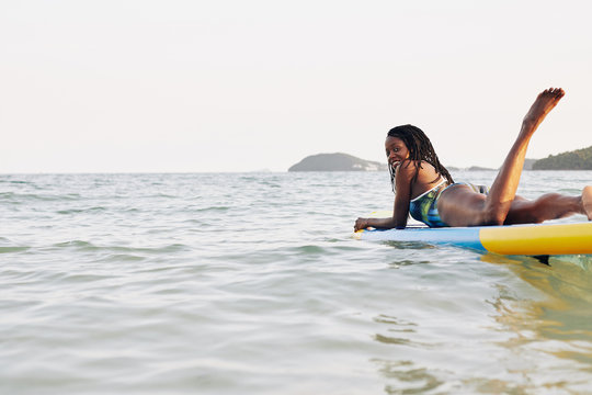 Happy attractive young Black woman lying on sup surfing board and looking at camera