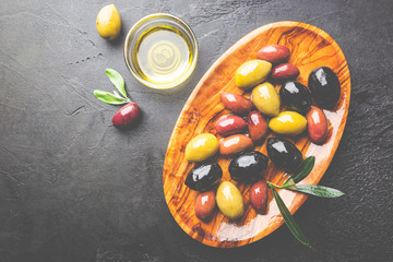 Black and green olives and olive oil in wooden bowls on black background. Top view with copy space...