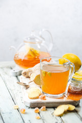 Ginger tea in a glass cup with lemon and mint on light background