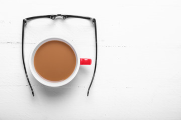 Cup of coffee with eyeglasses on white wooden background