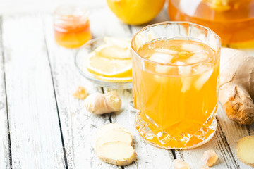 Yellow drink with ginger, lemon and ice in a glass, refreshing homemade ginger lemonade or ale on white background