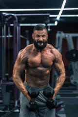 Muscular athletic bodybuilder working hard in gym on dark background