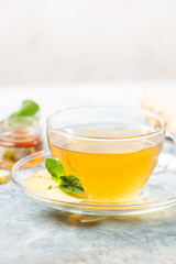 Ginger tea in a glass cup with lemon and mint on light background