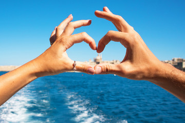 A young couple making heart with hands in rings,symbol of love  from the boat  at beautiful view on Valletta ,Malta