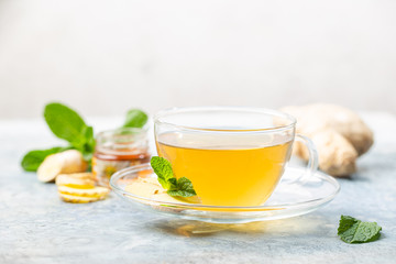 Ginger tea in a glass cup with lemon and mint on light background