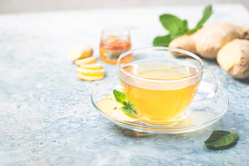 Ginger tea in a glass cup with lemon and mint on light background
