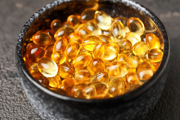 Bowl with fish oil capsules on grey background