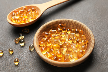 Bowl and spoon with fish oil capsules on grey background