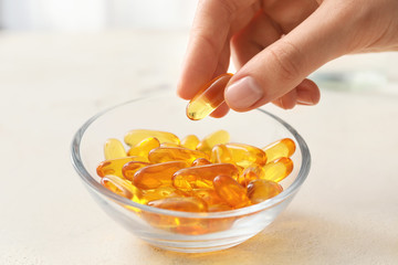 Woman taking fish oil capsule from bowl on table