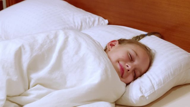 Happy girl teenager sweet dreaming in white bed in cozy bedroom. Smiling young girl sleeping sweetly at morning in home bed