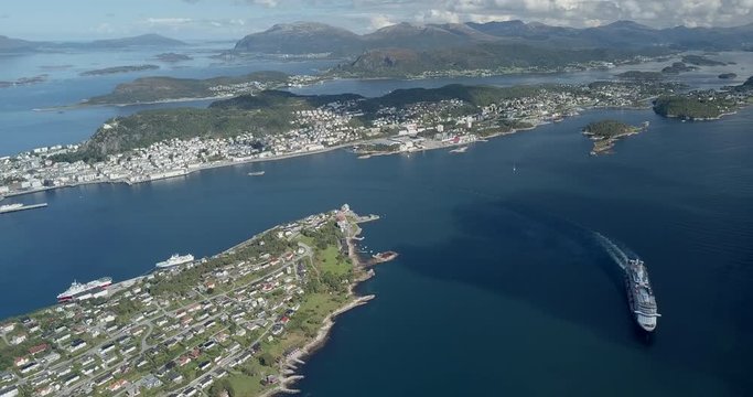 Extremely cinematic, high altitude aerial drone footage of a luxurious cruise ship sailing in a fjord next to Alesund, the most beautiful Art Nouveau town in Norway.