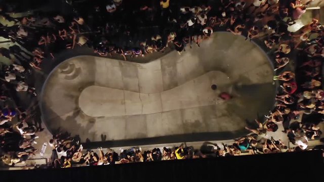 Aerial, rising, drone shot top down above a crowd watching a skater, doing tricks, in a skate park, during night time, in Bali, Indonesia