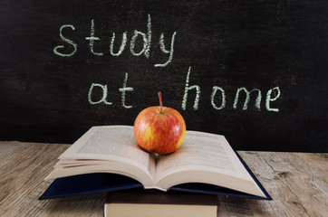 An apple on an open book. The inscription on the board "study at home." The concept of distance education. Quarantine.